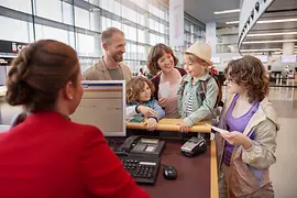 Una joven familia con tres niños en el mostrador de facturación de Austrian Airlines del aeropuerto de Viena